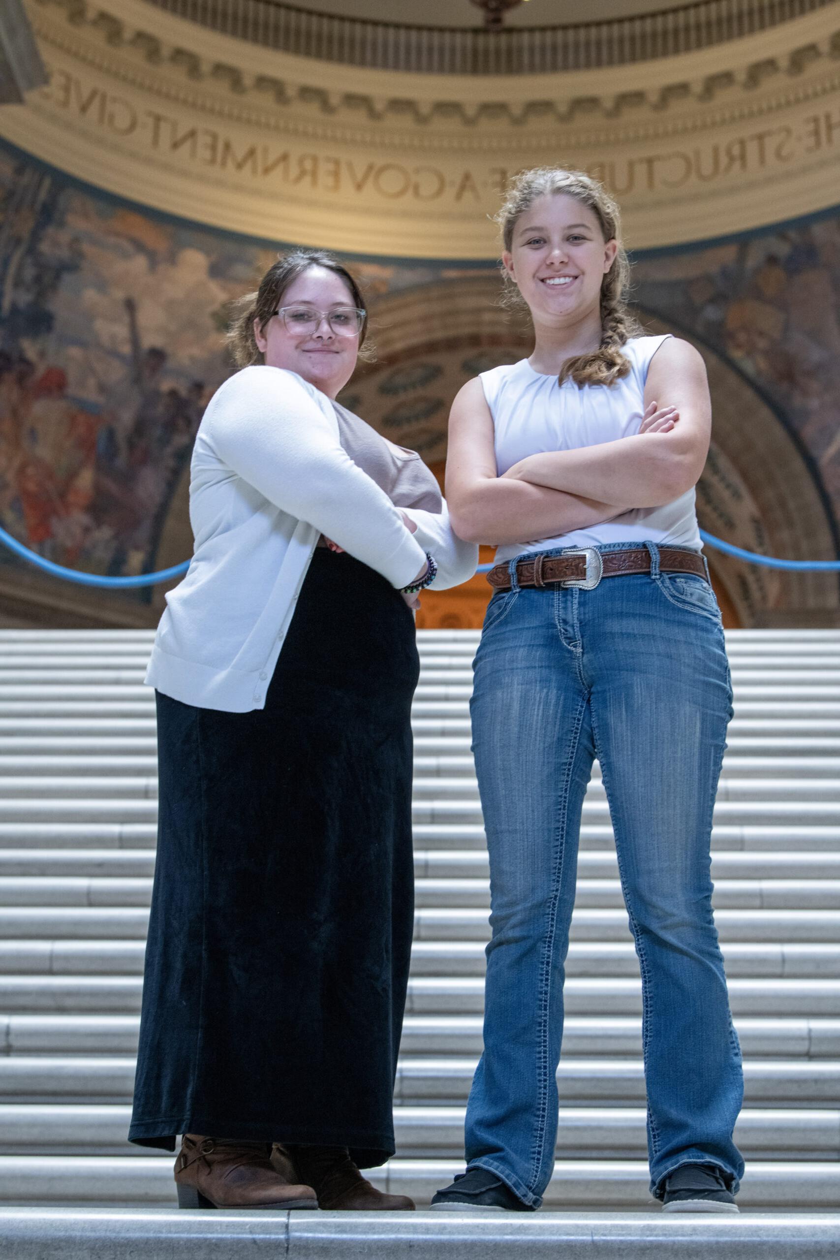 Two students posing with their arms crossed on the steps of a government building